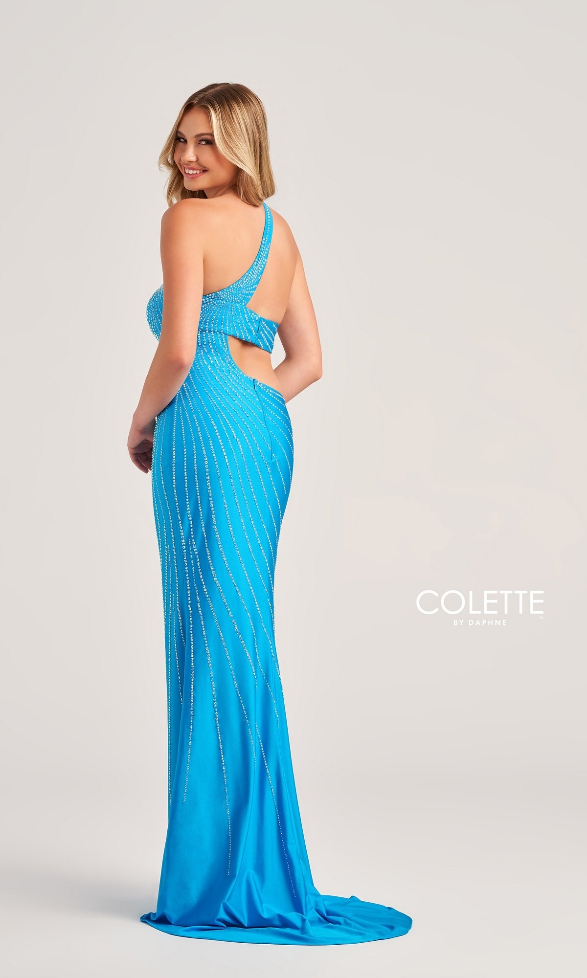 Woman in a blue Colette One-Shoulder Sleek Long Prom Dress CL5139 with beaded stripes and a side cutout, standing and smiling over her shoulder.